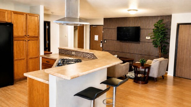 A modern kitchen with wooden cabinets, a gas stove, a stainless steel range hood, and a bar area with stools. - Manitou Pikes Peak Hotel (Manitou Springs)