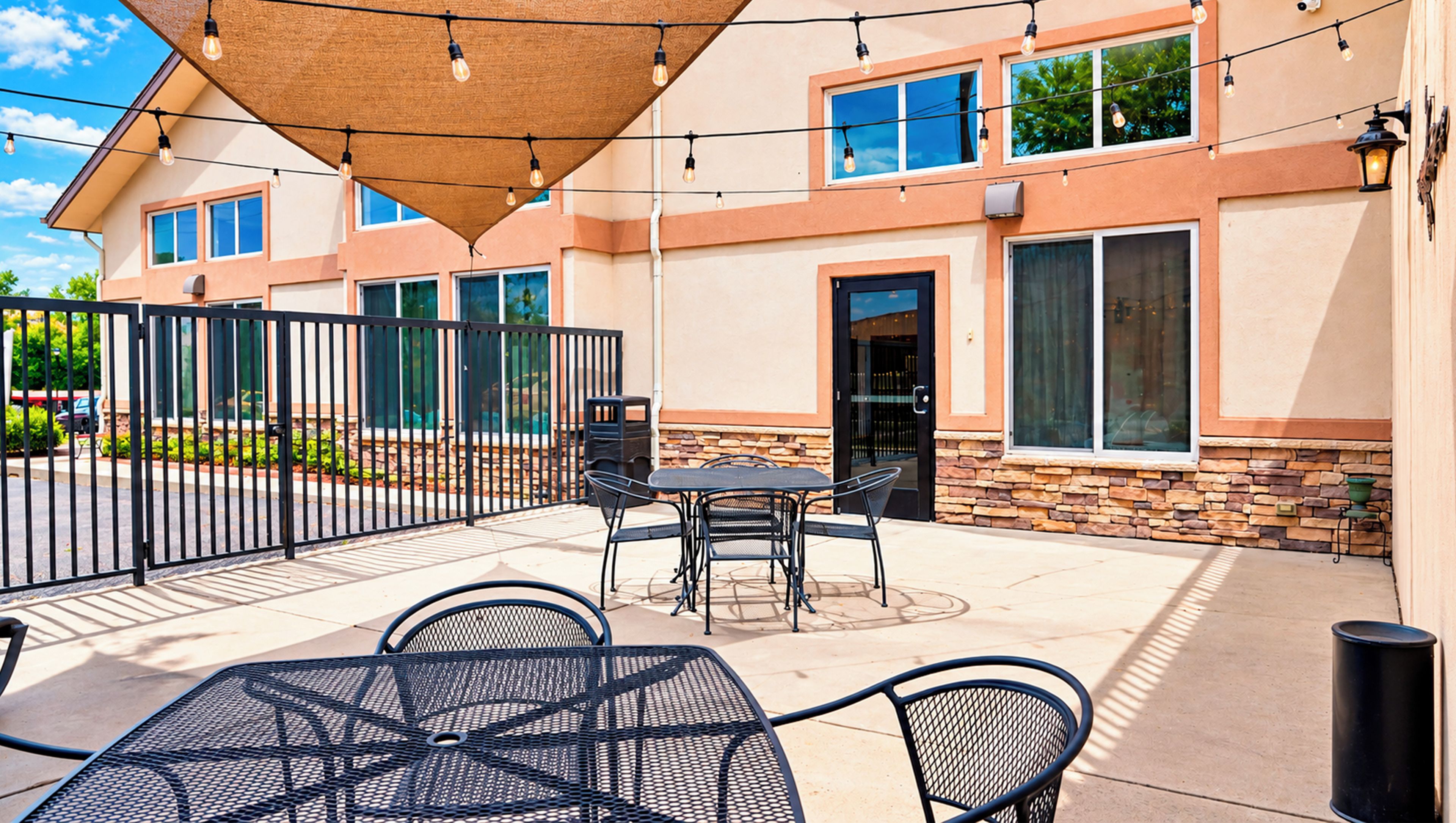 Un patio exterior con una mesa, sillas, una puerta y un edificio con ventanas y fachada de piedra.