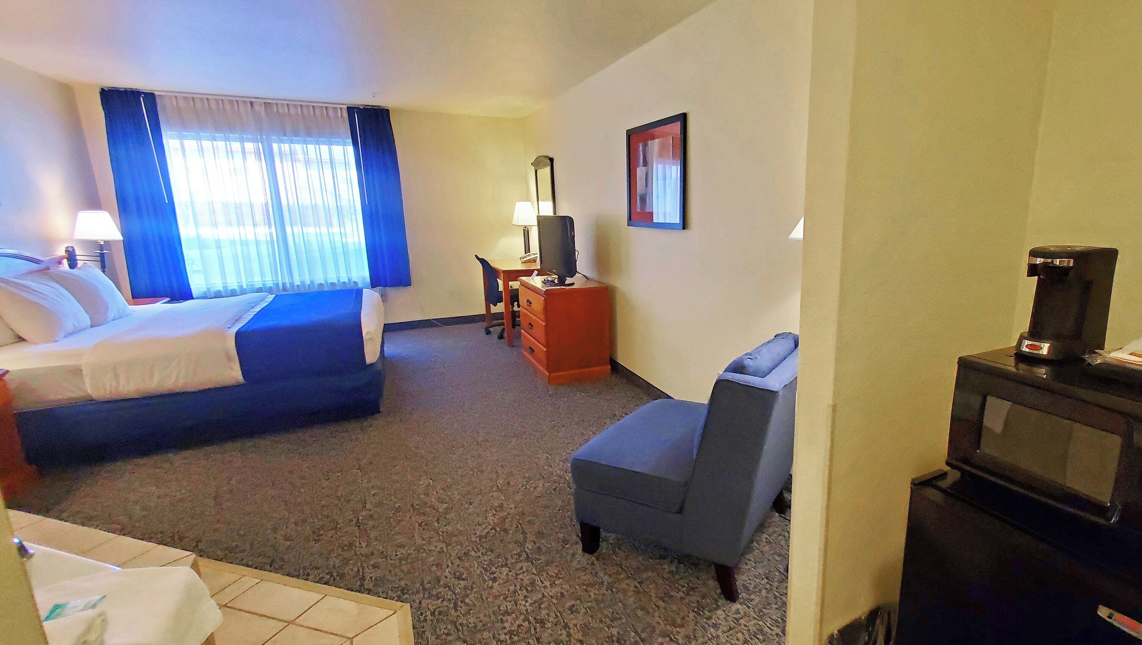 A hotel room with a bed, a desk, a chair, a television, and a coffee machine.