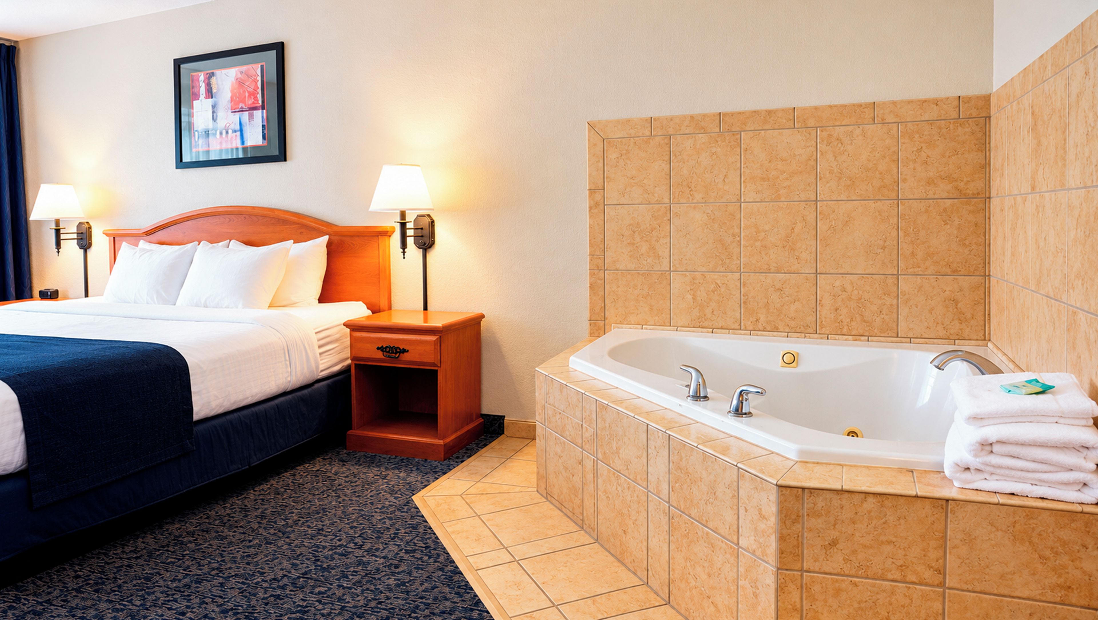 A hotel room with a bed, bedside lamps, a nightstand, a bathroom with a bathtub, and a towel stack.