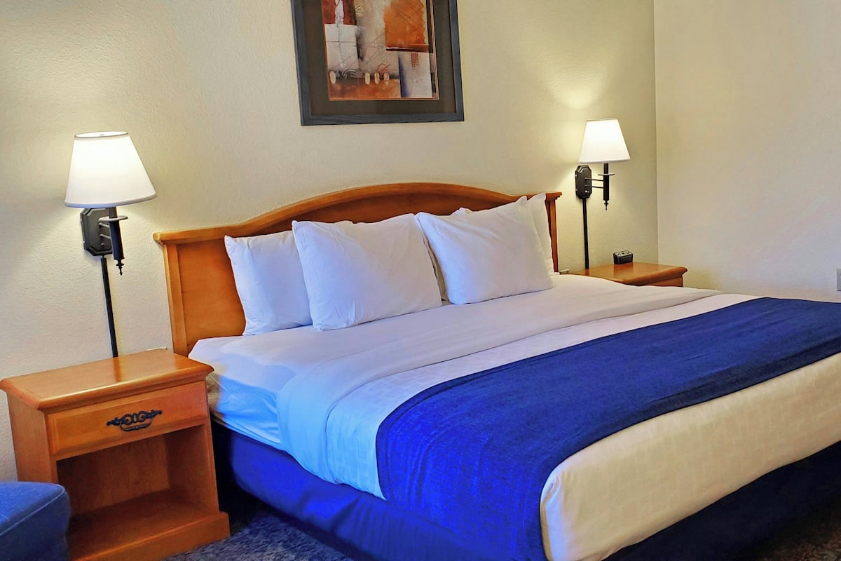 A hotel room with a bed, two bedside lamps, a nightstand, and a framed picture on the wall.