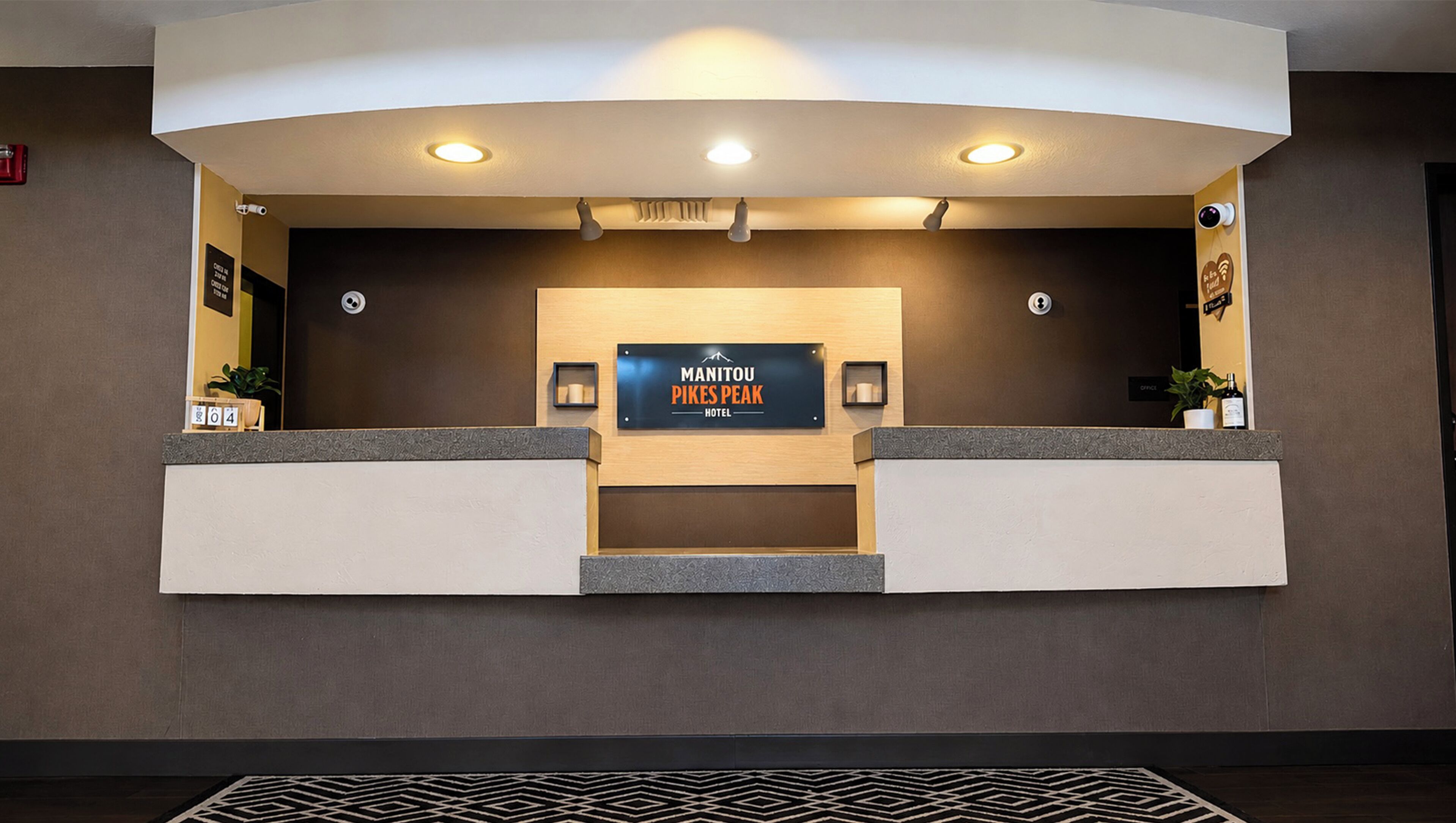 A reception desk with a sign for Manitou Pikes Peak Hotel, a security camera, and a potted plant.