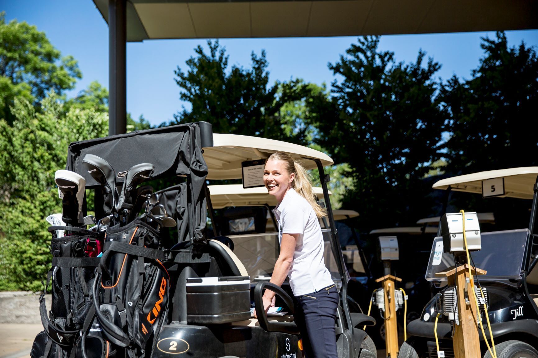 A golf cart with a person standing beside it, a golf bag, and a sign with the number 5.