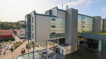 Un bâtiment moderne doté d’une terrasse sur le toit, d’un plan d’eau à l’avant et d’une cour avec des espaces de détente en plein air.