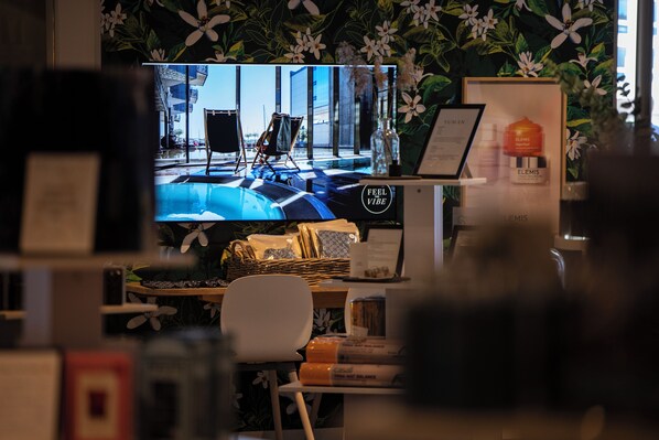 A room with a television displaying an outdoor scene, a desk with a basket, a chair, and a framed picture.