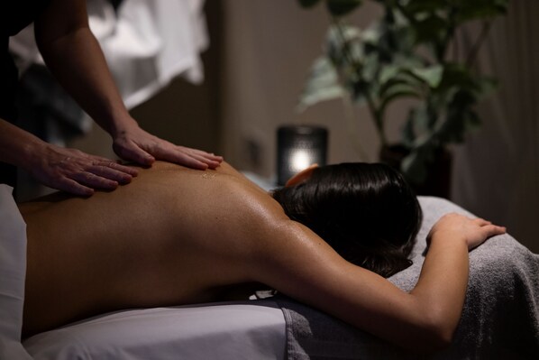 A massage therapy session in a dimly lit room with a massage table, towels, and a potted plant.