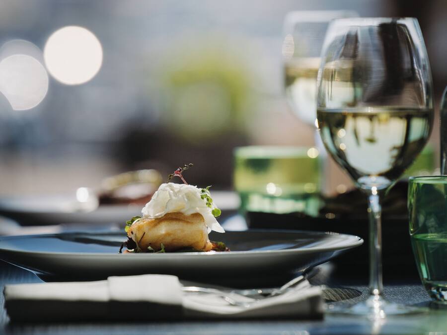 A dining table with plates, a glass of white wine, and a dessert.