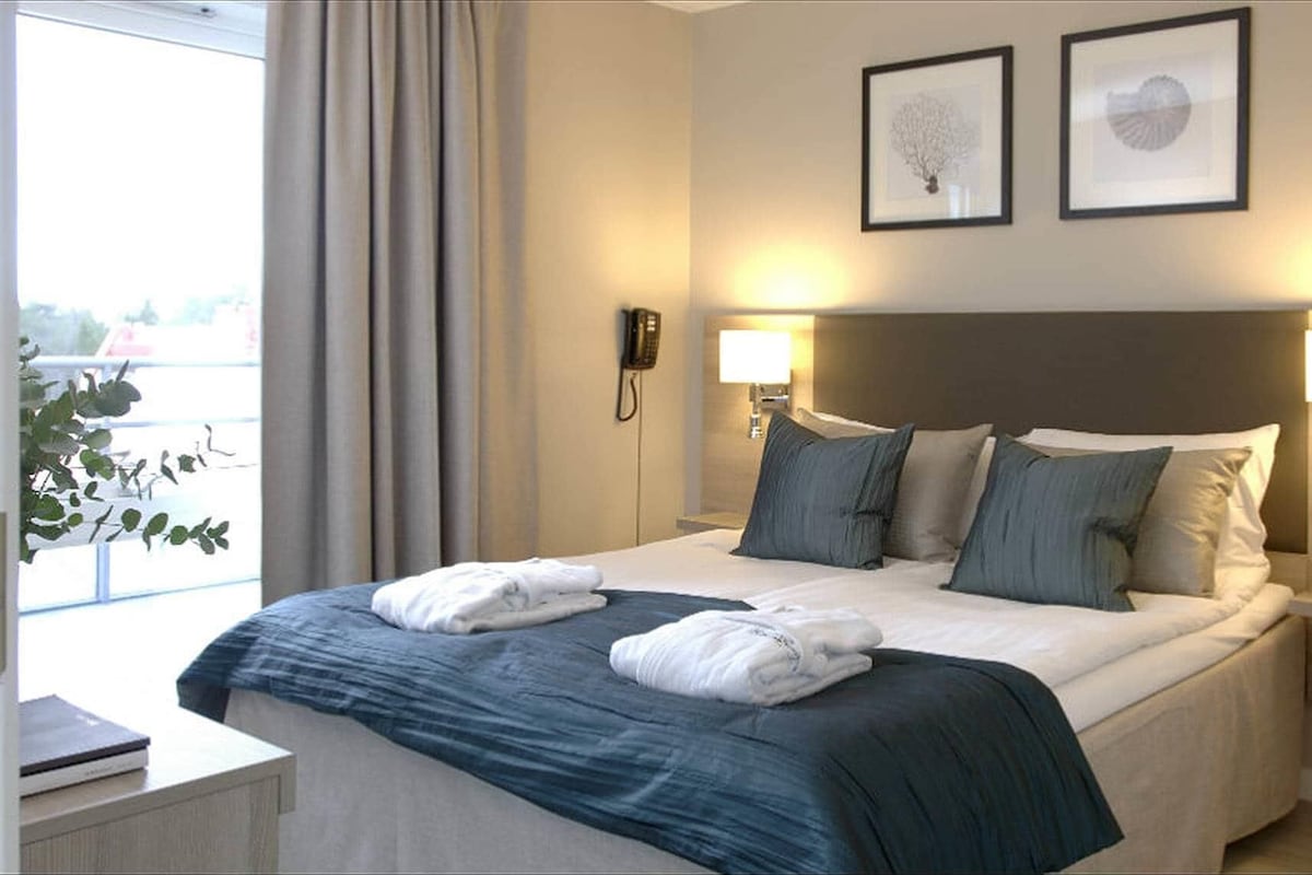 Una habitación de hotel con una cama grande, dos lámparas de noche, un teléfono y dos cuadros en la pared.
