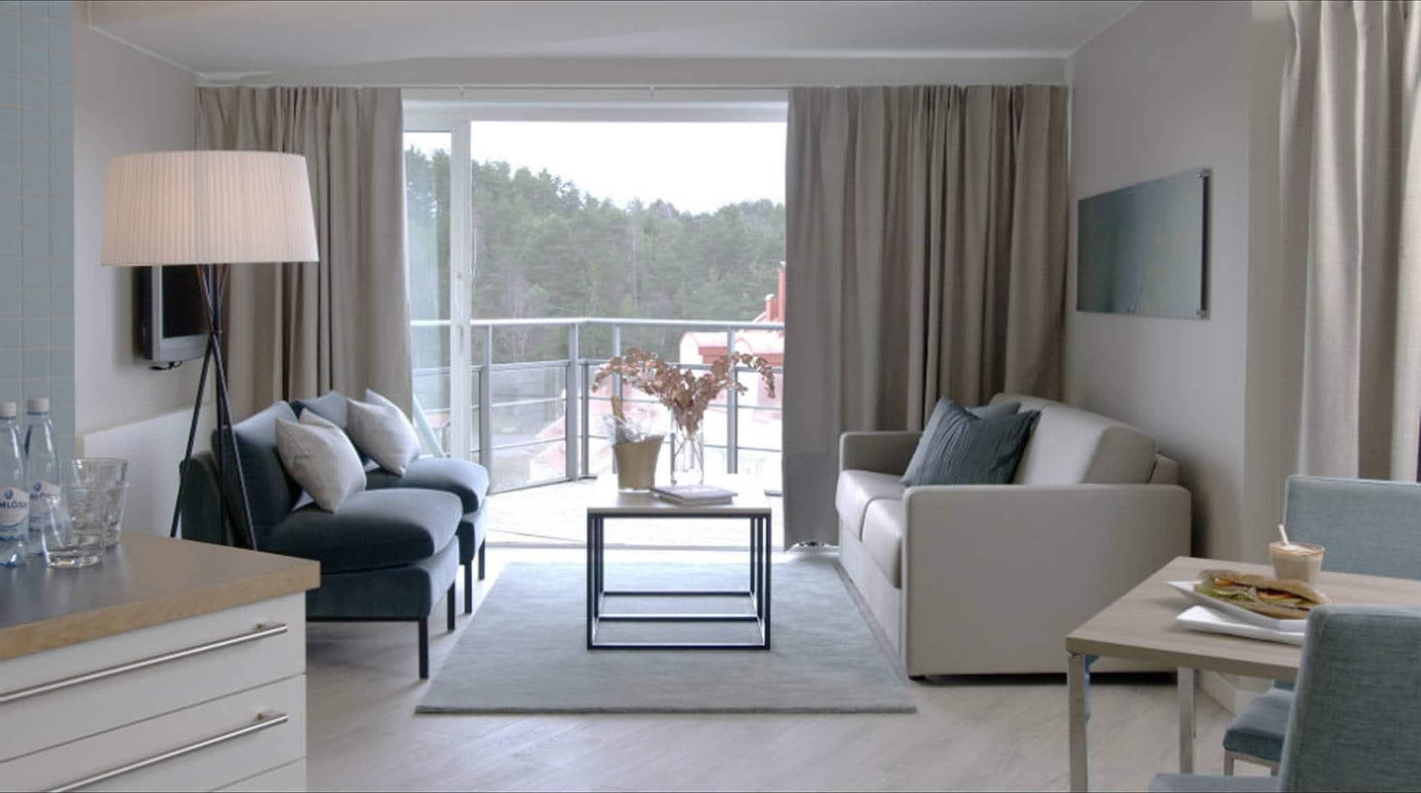 Una sala moderna con un sofá, una mesa de centro, un televisor y un balcón con vistas a árboles.