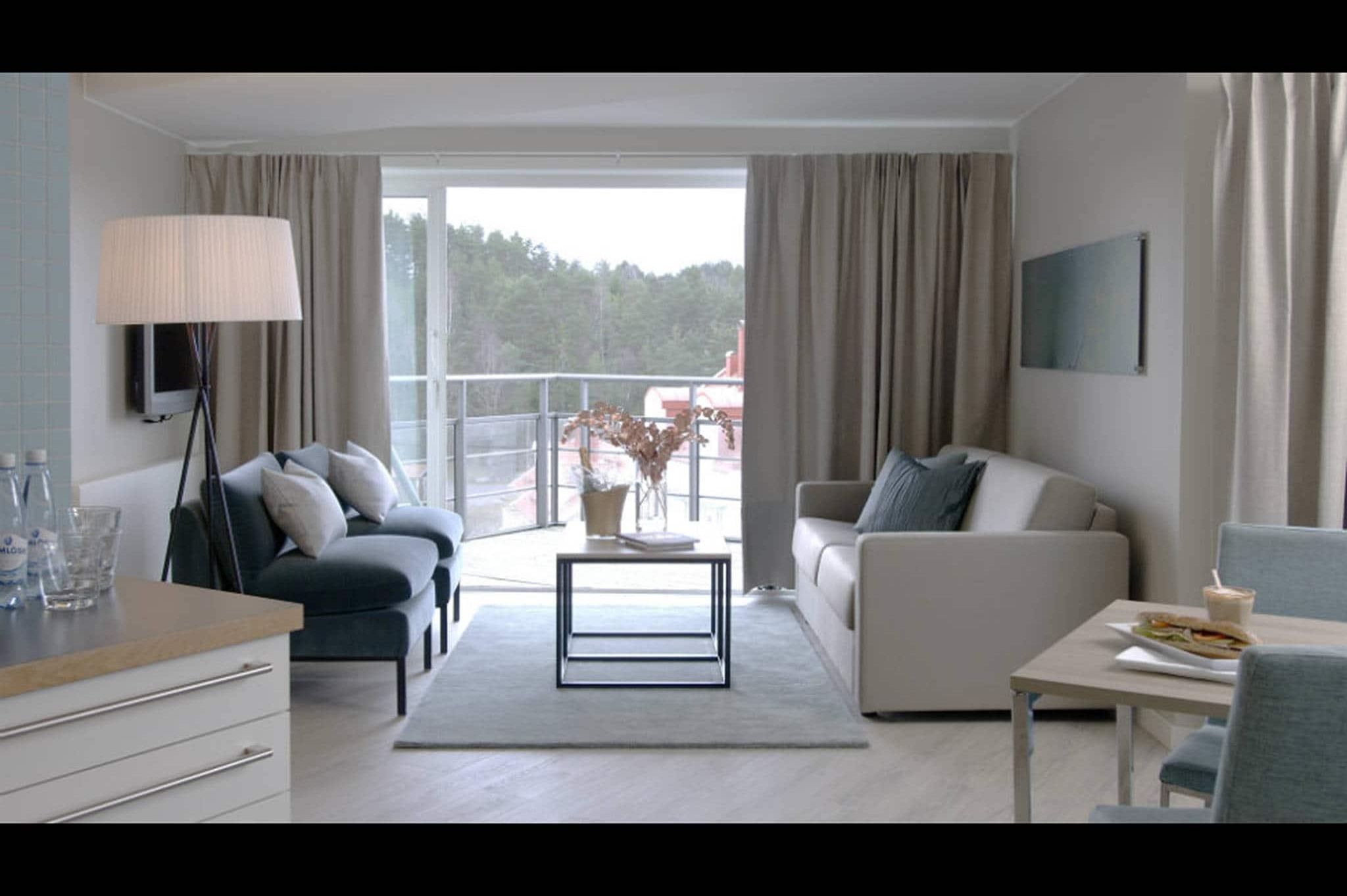 Una sala moderna con un sofá, una mesa de centro, un televisor y un balcón con vistas a árboles.