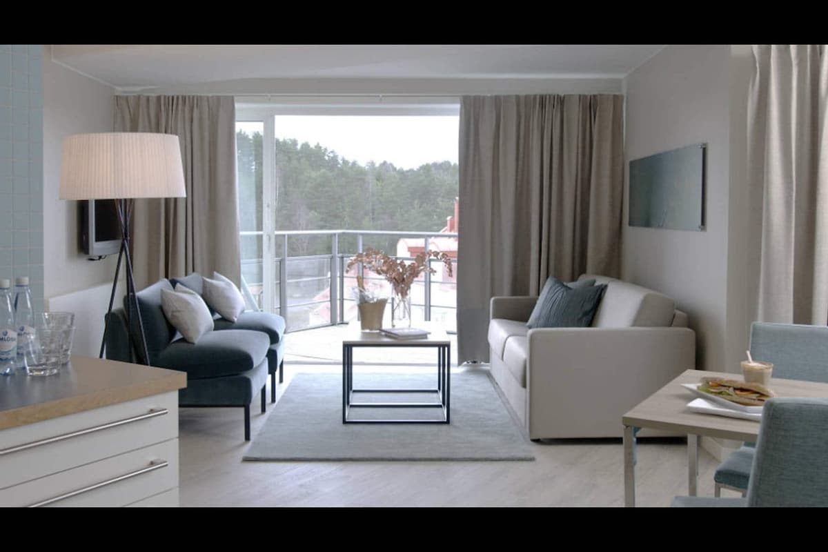 Una sala moderna con un sofá, una mesa de centro, un televisor y un balcón con vistas a árboles.