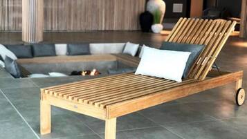 A wooden lounge chair with wheels, a grey sofa, and a decorative vase in a modern lobby.