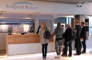 Un espace d’accueil à Kragerø Resort, avec un comptoir de réception en bois, une enseigne au-dessus et quelques personnes qui se tiennent à proximité.