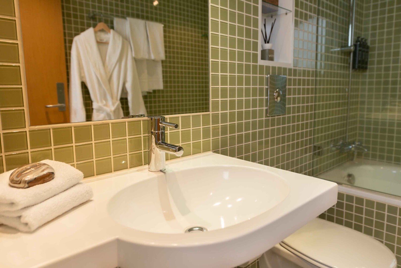 Un baño con lavamanos blanco, espejo, toalla y cabina de ducha con vidrio.