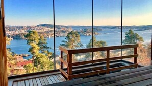 A room with a wooden bench and large windows offering a view of a lake and a cityscape.