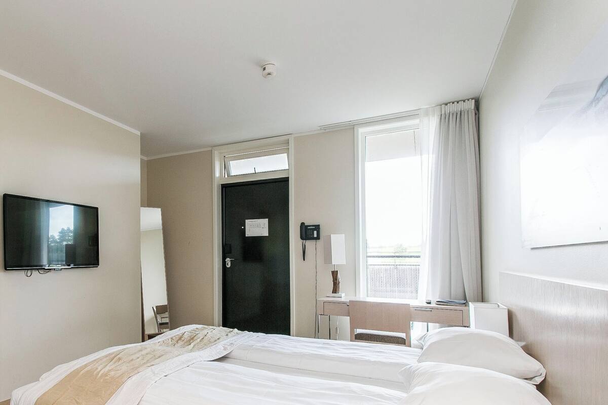 A hotel room with a bed, a desk, a chair, a television, and a window with curtains.