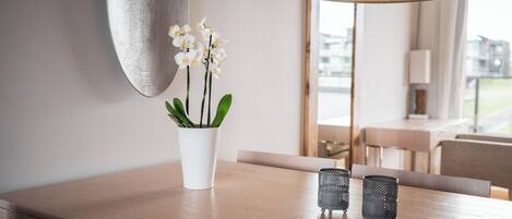 A modern dining area with a wooden table, a white vase with orchids, and two metal candle holders.