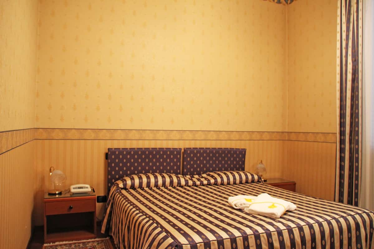 A hotel room with a striped bedspread, two pillows, a bedside table with a lamp, and a telephone.