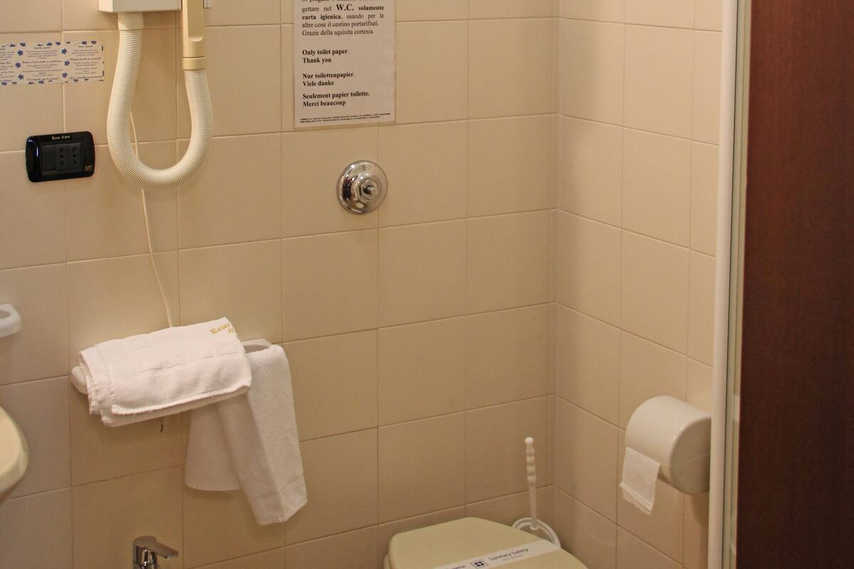 A small bathroom with a toilet, sink, and shower. There is a paper towel dispenser, a hand dryer, and a sign with instructions.