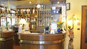 Zona de recepción de un hotel con un mostrador de madera, un reloj, un bar con diversas botellas y una estatua de una persona sosteniendo una antorcha.