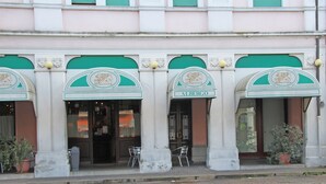 Fachada de edificio con tres portales arqueados, cada uno con una mesa y una silla afuera, y con la leyenda 'ALBERGO'.