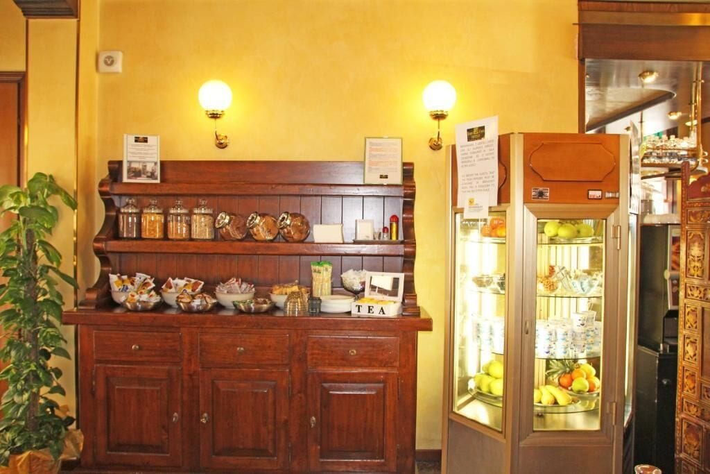 A wooden counter with jars and a tea sign, a refrigerator with fruits, and wall-mounted lights.