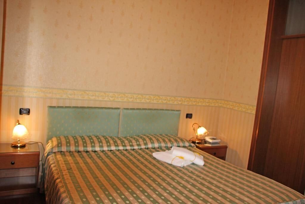 A hotel room with a bed, two bedside lamps, a nightstand, and a wooden wardrobe.