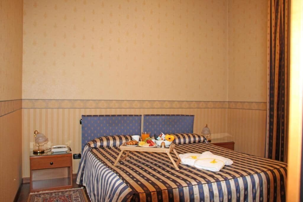 Une chambre d’hôtel avec un lit, une table de chevet et une petite table sur laquelle sont disposés des articles pour le petit-déjeuner.