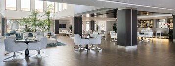 A spacious lobby with modern seating, a bar area, and large windows allowing natural light.