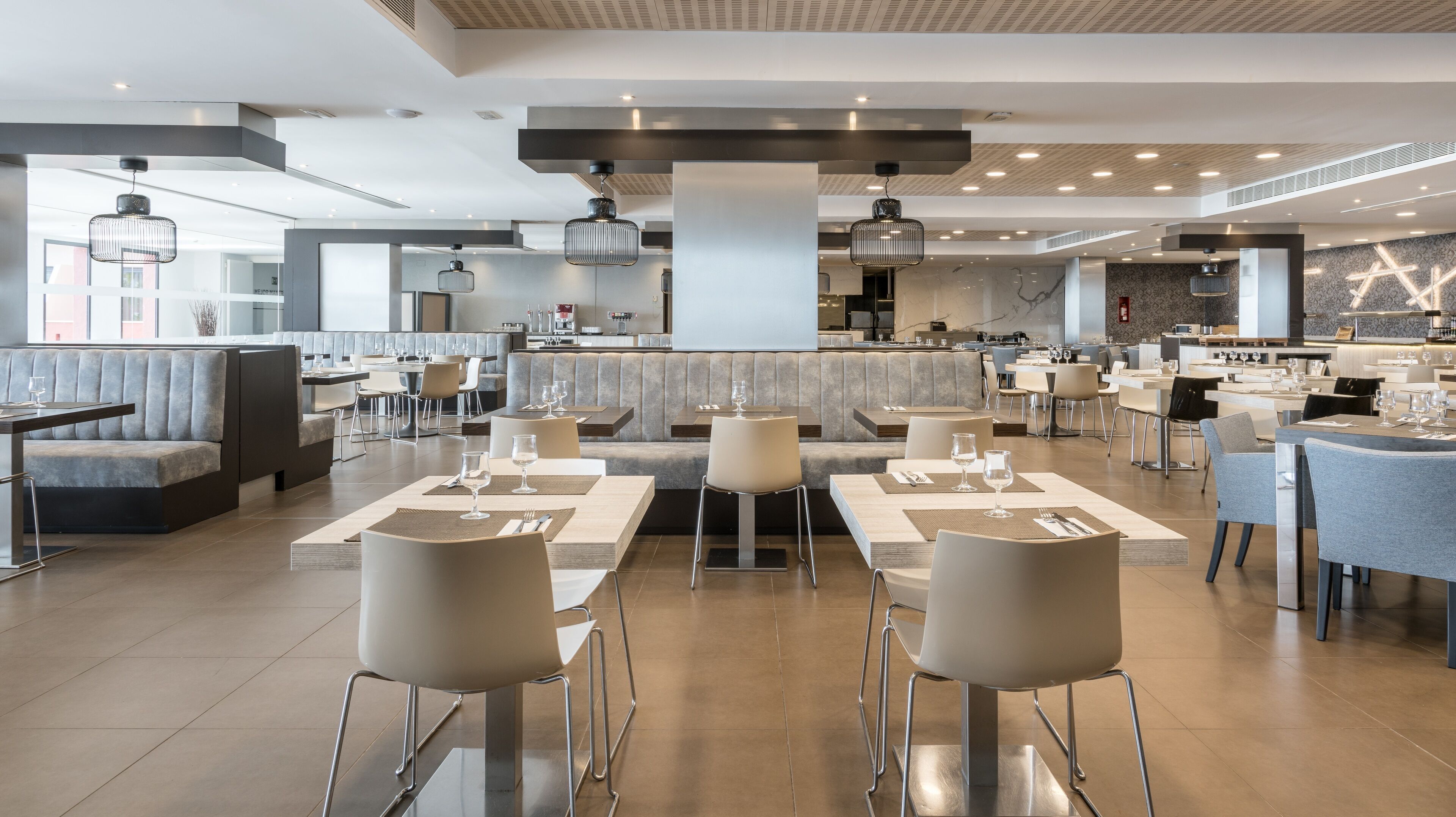 Ein modernes Restaurant mit hohen Tischen, Sitzgelegenheiten in Kabünen, einer zentralen Bar und Blick auf die Küche.