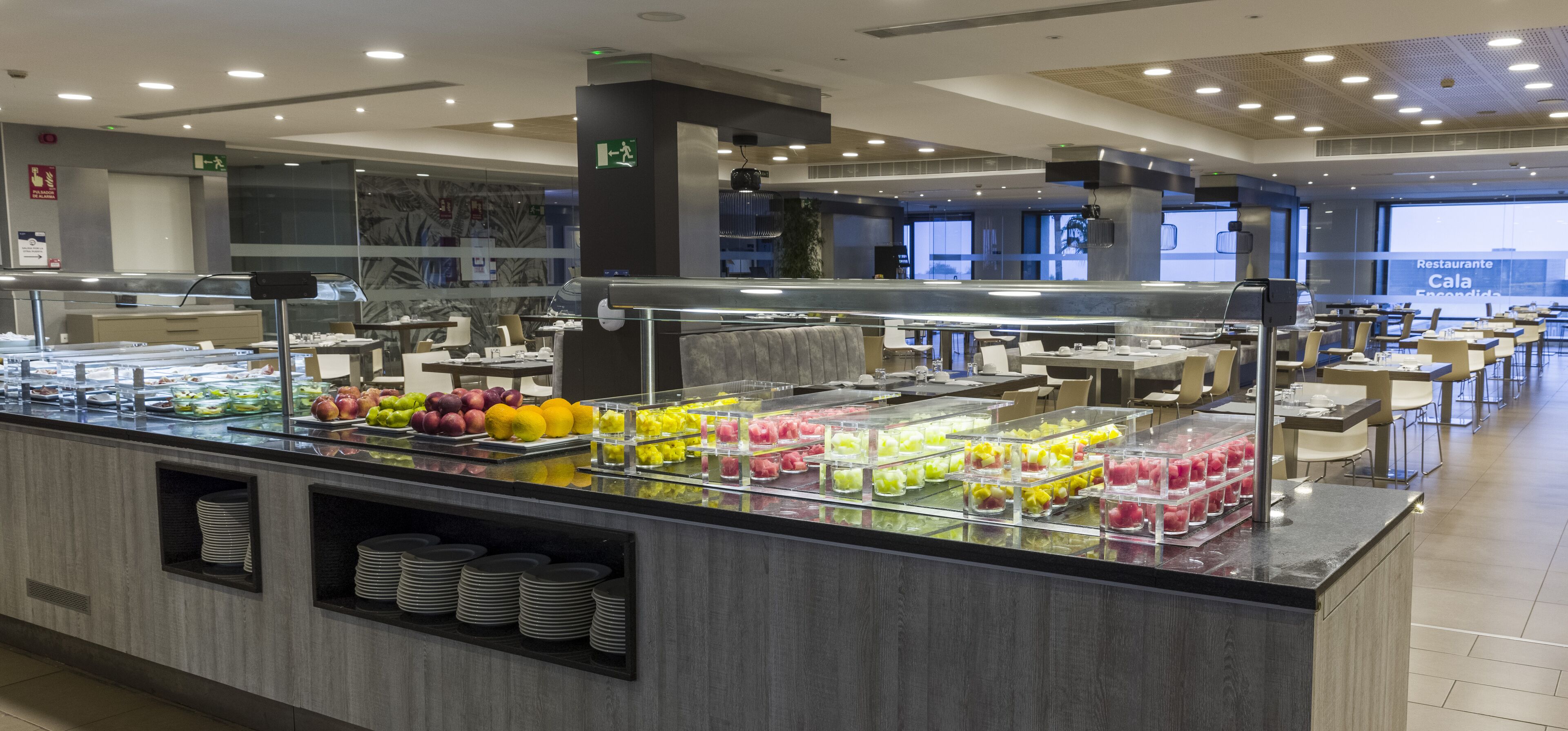 Un área de bufé con diversos alimentos y un espacio de estar con mesas y sillas.