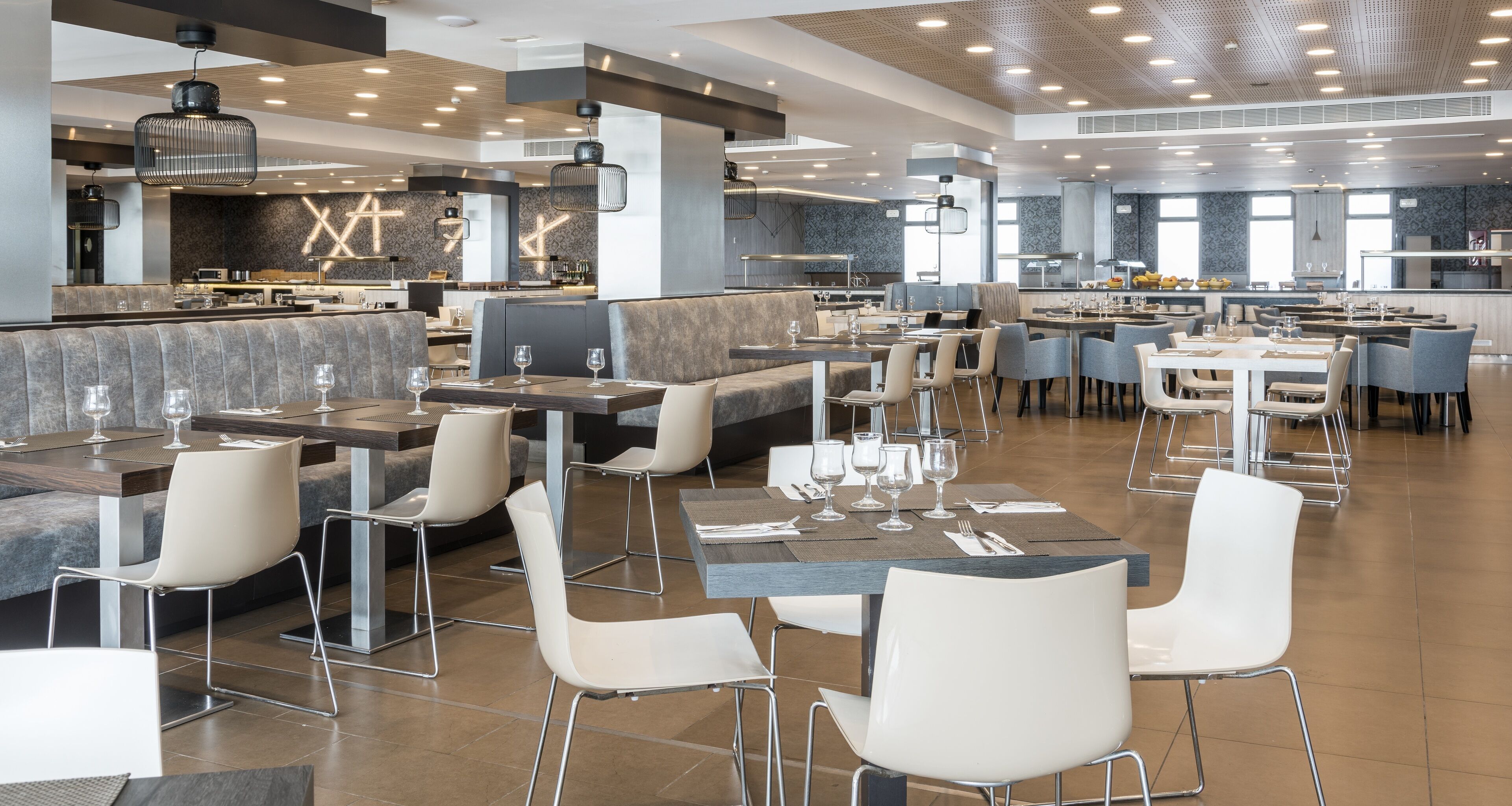 A modern restaurant with high tables and booths, a bar area, and a kitchen in the background.