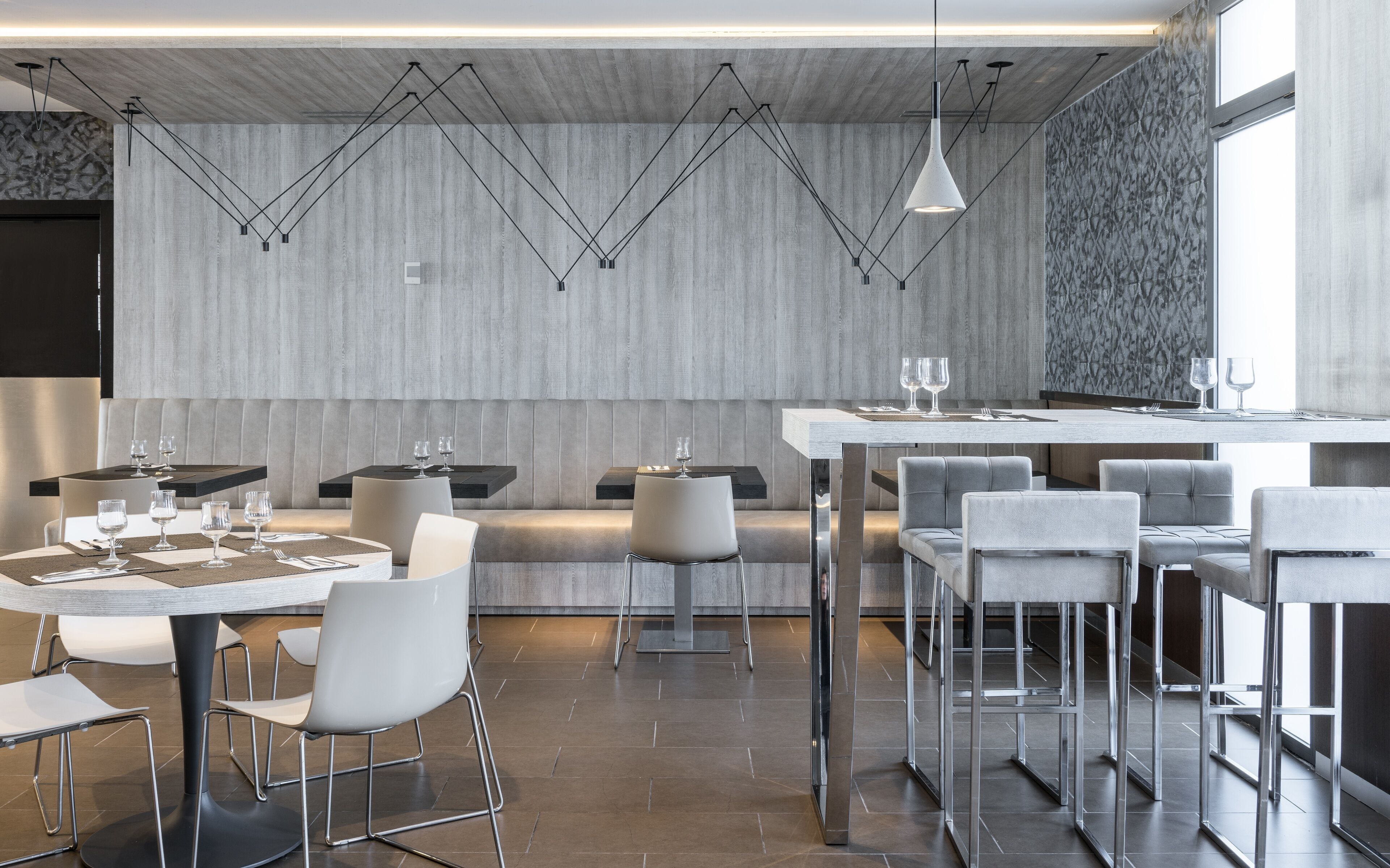 Un restaurant modern amb taules i cadires altes, il·luminació penjant i un mur de pedra de fons.