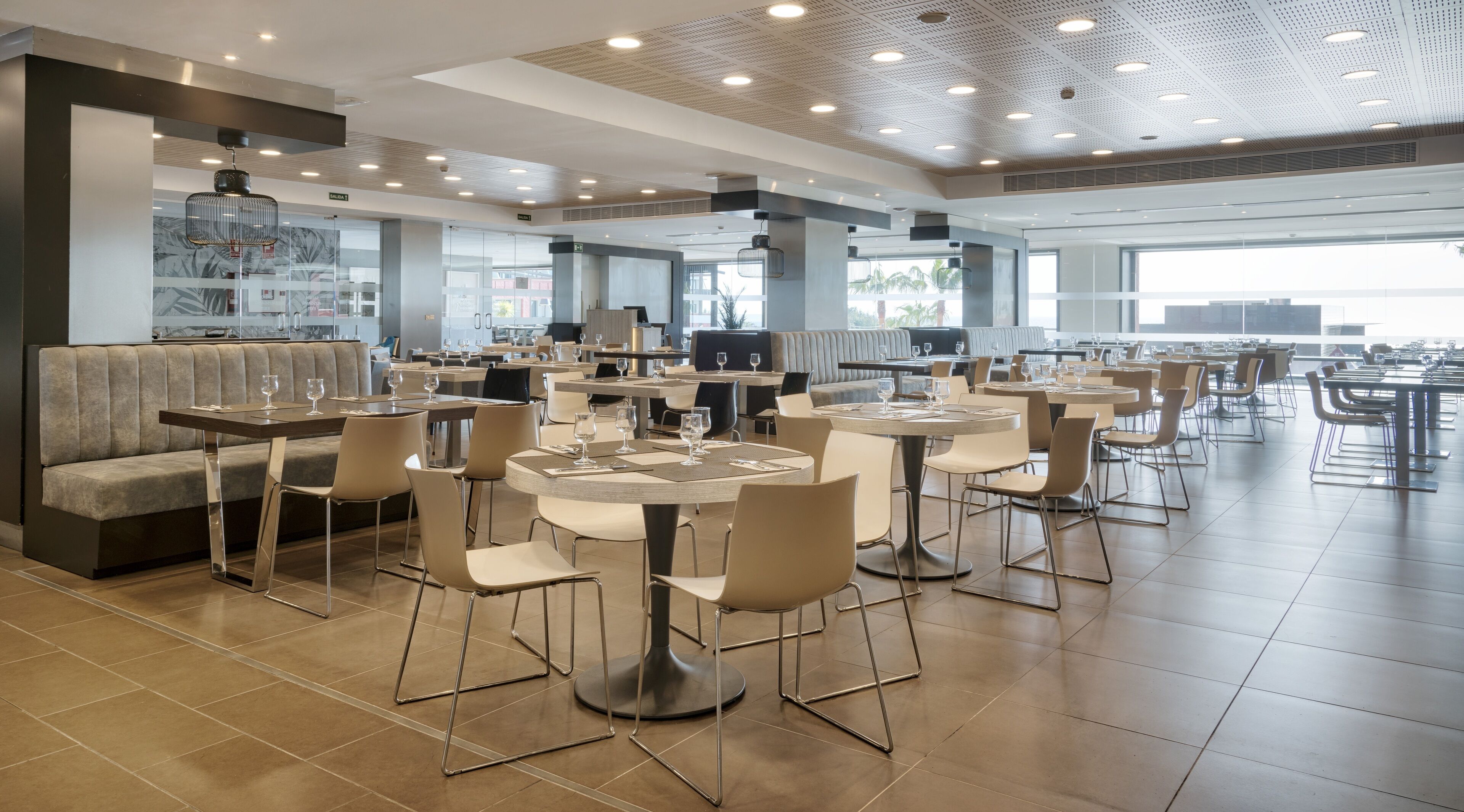 A modern restaurant with round tables and chairs, a bar area, and a seating section with a sofa.