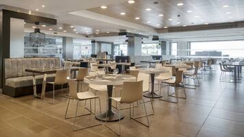 A modern restaurant with round tables and chairs, a bar area, and a seating section with a sofa.