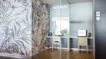 A modern hotel lobby with a glass partition labeled "INTERNET," two computer stations, and a decorative wall with a tropical leaf pattern.