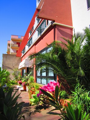 A multi-story building with balconies, surrounded by lush greenery and potted plants. - La Piramide (Roccalumera)