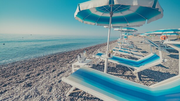 Una platja amb files de gandules i ombrelles.