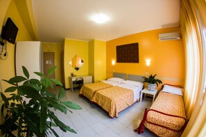 A hotel room with two beds, a desk, a chair, a potted plant, and an air conditioning unit. - La Piramide (Roccalumera)
