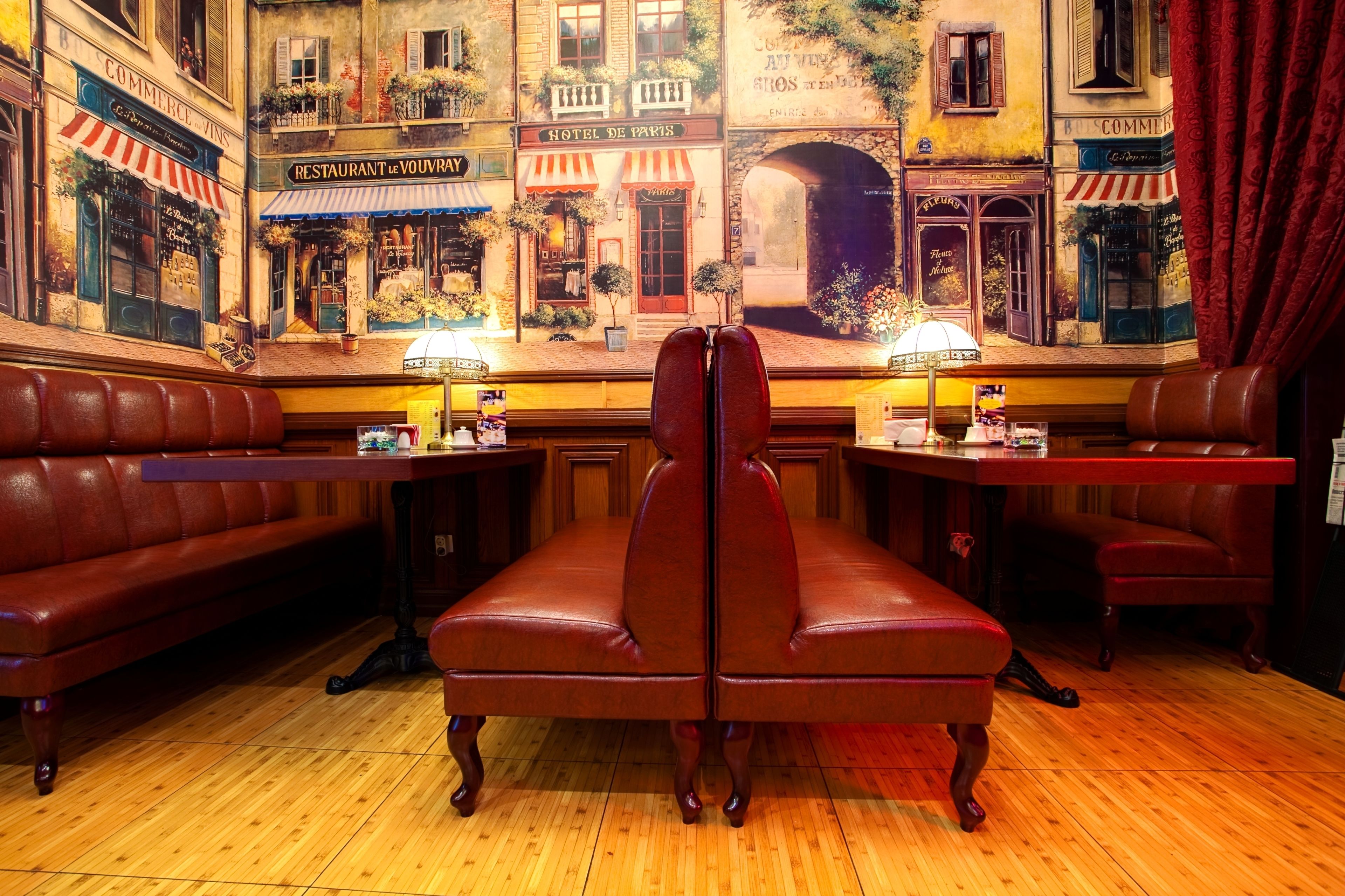 A restaurant with a bar area, wooden flooring, and a mural of Parisian buildings.