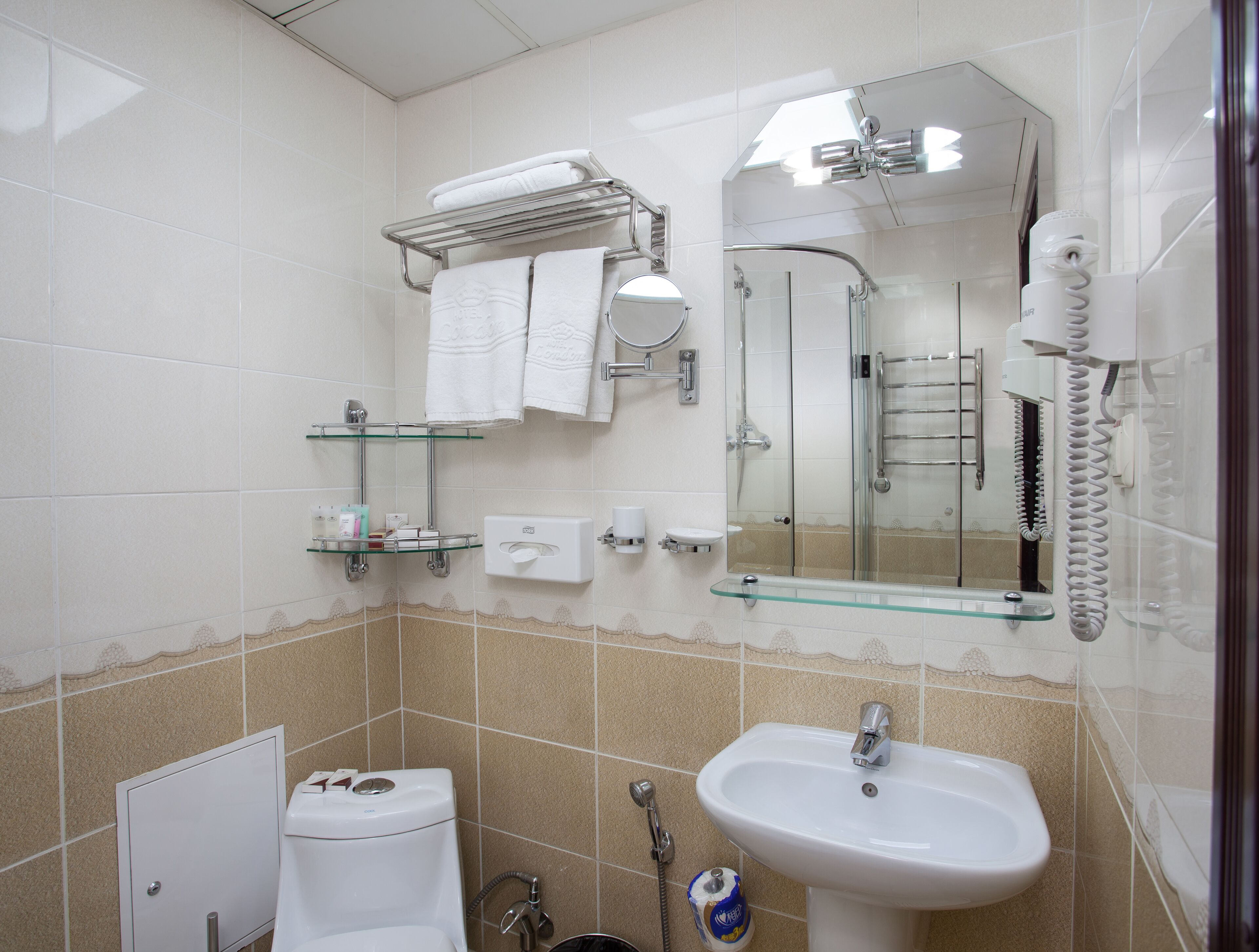 A bathroom with a toilet, sink, and shower. There are towels and toiletries on shelves.