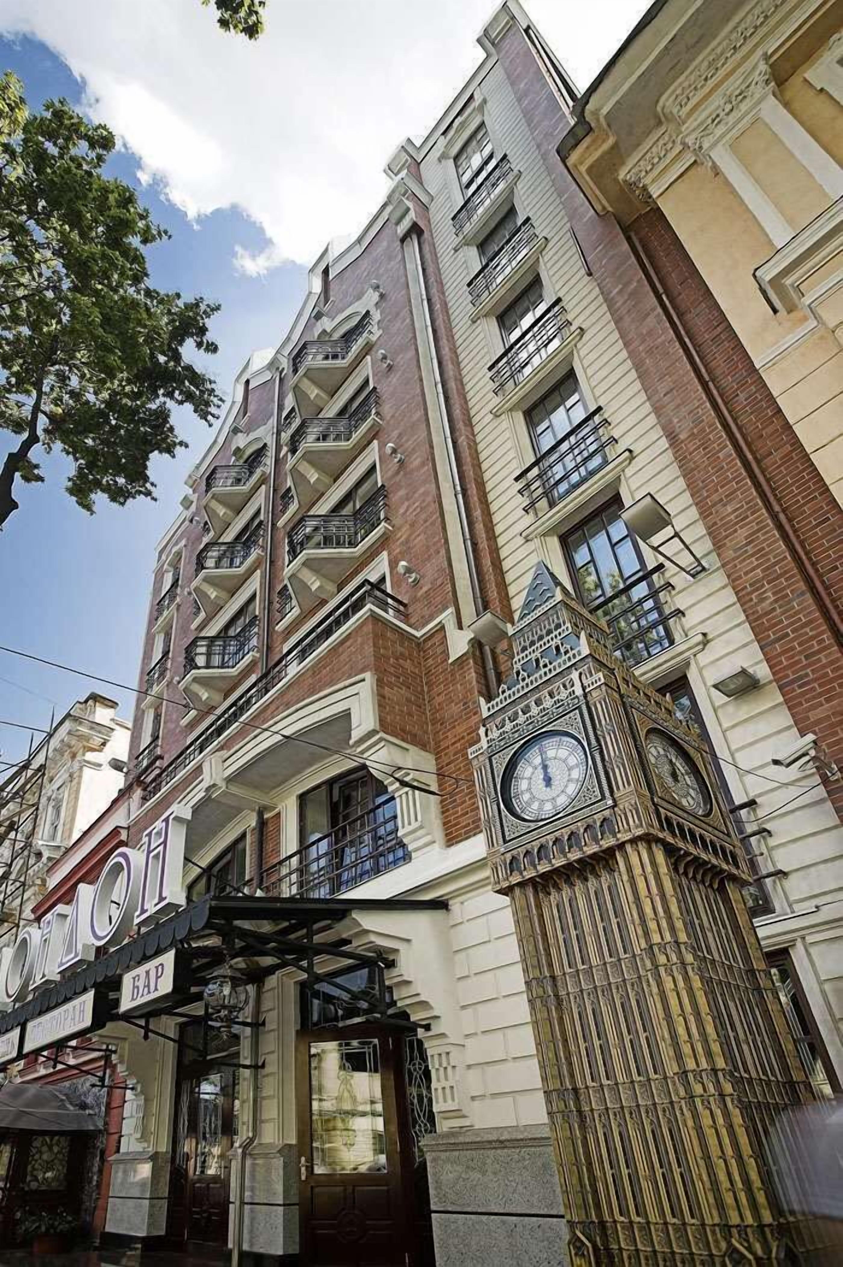 Un edificio de varios pisos con una imponente torre de reloj, balcones y una tienda con rótulos.