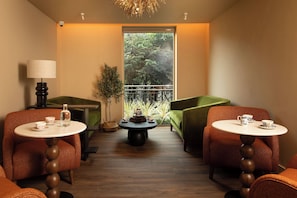 A room with two round tables, two chairs, a lamp, a potted plant, and a view of trees through a window. - The Address Citywest (Dublin)