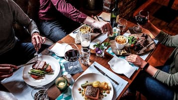 Un grupo de personas cenando en una mesa de madera con varios platos, incluyendo filete y verduras, y copas de vino.