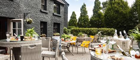 Un patio al aire libre con muebles de mimbre, una mesa preparada con comida y bebidas, y botellas de vino.
