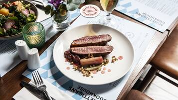 Une assiette de magret de canard avec sa sauce et des légumes, un verre de bière et un menu sur une table en bois.