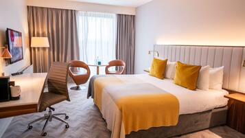 A hotel room with a large bed, two chairs, a desk with a lamp, and a painting on the wall.