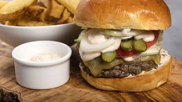 A burger with pickles, onions, and a bun, accompanied by a side of fries and a small container of sauce.