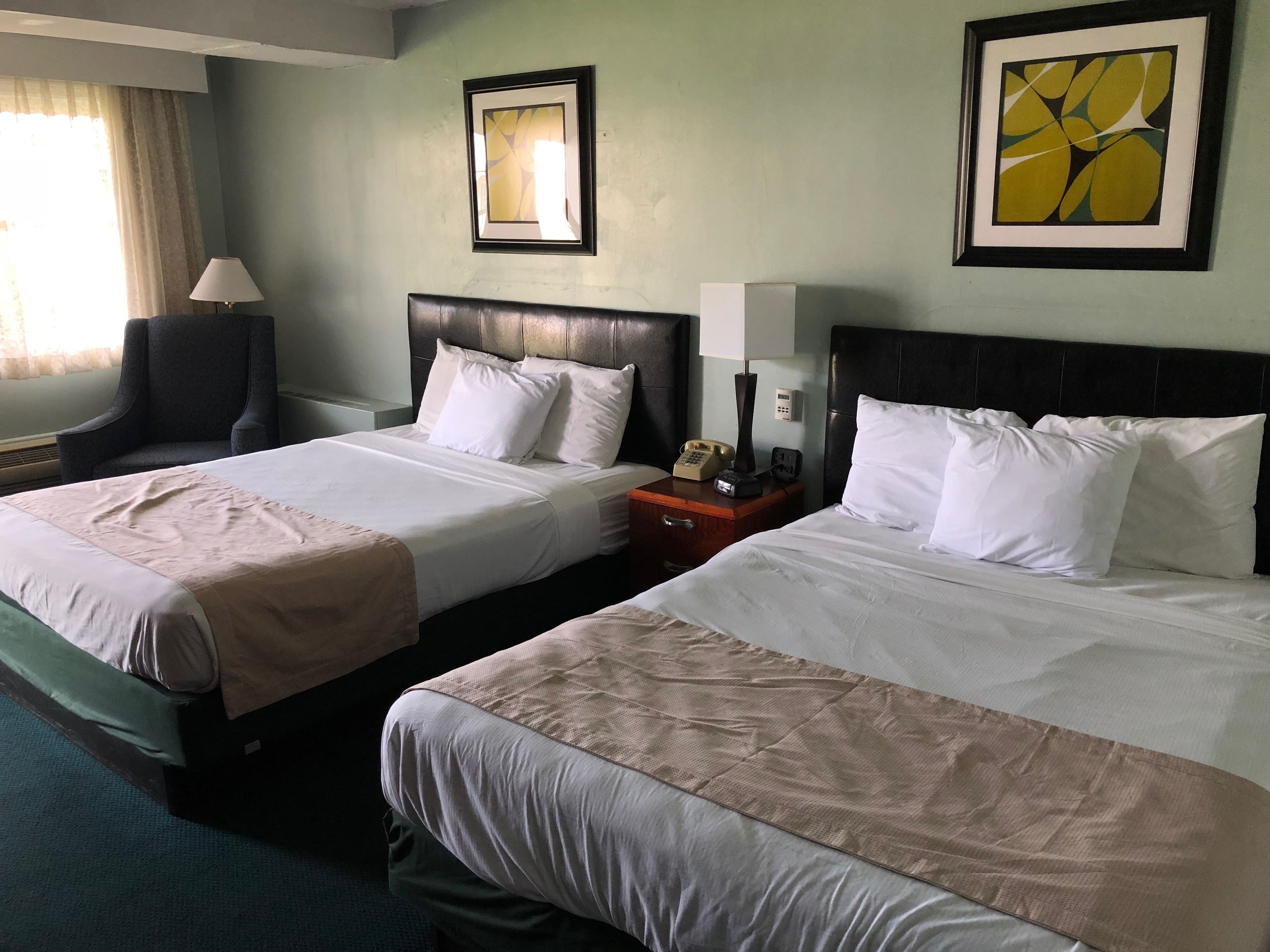 Habitación de hotel con dos camas, una mesita de noche con teléfono, una lámpara y cuadros en las paredes.
