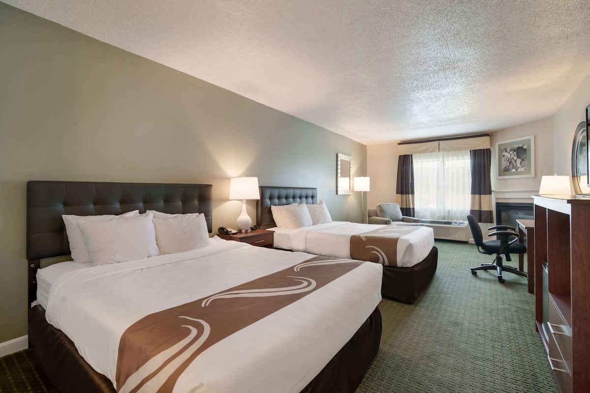 Quarto de hotel com duas camas, uma mesa, uma cadeira e uma televisão.